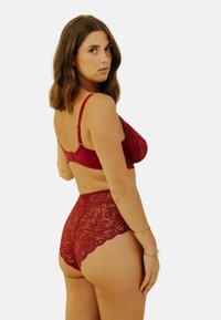 Soutien-gorge en dentelle rouge avec bretelles réglables et culotte taille haute assortie. Présente des motifs floraux et des bords festonnés pour plus de détails.