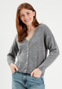 Cardigan grigio lavorato a maglia con scollo a V, maniche lunghe e chiusura a cinque bottoni. Presenta una consistenza morbida e una vestibilità casual. Indossato su jeans blu.