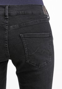 Czarne dżinsy o slim fit, z tylnymi kieszeniami z subtelnie wykończonym szwem oraz skórzaną metką na talii. Miękka tekstura.