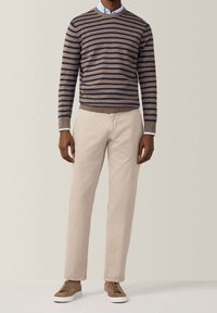 Braun gestreifter Pullover, khakifarbene Hose und beige Turnschuhe. Der Pullover hat einen Rundhalsausschnitt und gerippte Bündchen. Die Hose ist gerade geschnitten und hat einen sauberen Abschluss.