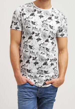 Hvid T-shirt med sort blomstermønster og kranier, korte ærmer og rund halsudskæring, kombineret med blå cowboybukser.