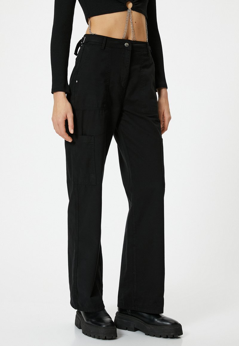 Pantaloni cargo neri con una vestibilità rilassata, dotati di tasche laterali e una texture di tessuto liscia. Indossati con robusti stivali neri alla caviglia.