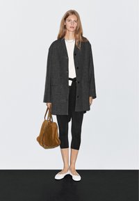 Szary, oversize'owy płaszcz z guzikami na białej bluzce i czarnych legginsach, w zestawieniu z białymi balerinami i brązową torebką ze zamszu. Teksturowane materiały.