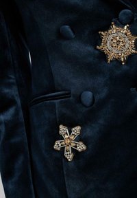 Marine fluwelen kledingstuk met twee sierlijke broches: een ronde gouden en edelstenen design en een stervormige broche met sprankelende accenten.
