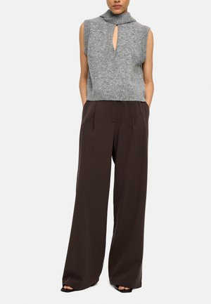 Bezrekawnik szary dzianinowy z dekoltem w kształcie łezki, zestawiony z luźnymi, ciemnobrązowymi szerokimi spodniami z wysokim stanem oraz czarnymi sandałami z odkrytymi palcami.