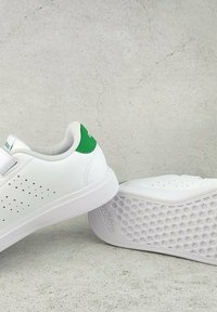 Baskets blanches avec des accents verts, en matériau synthétique, avec des côtés perforés et une semelle en caoutchouc texturée avec un motif hexagonal.
