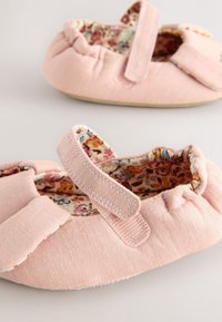 Chaussures bébé roses douces avec doublure intérieure fleurie et bandes auto-agrippantes réglables sur une surface gris clair.