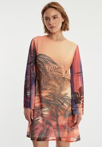 Robe à manches longues présentant un dégradé d'orange à violet, avec un motif de feuilles tropicales en noir, fabriquée dans un tissu lisse et léger.
