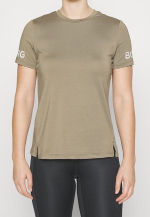 Kobieta w oliwkowo-zielonym T-shircie z krótkim rękawem z napisem „BORG” na rękawach i czarnych legginsach, widoczna od szyi do bioder.