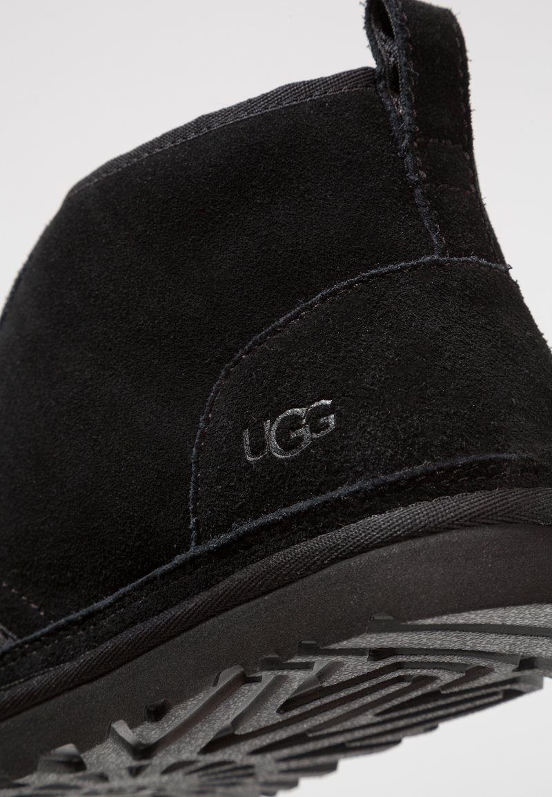 Black suede ankle boot with a textured sole, featuring a stitched seam and subtle UGG logo on the side.