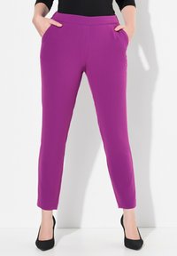 Pantaloni viola aderenti e elasticizzati con tasche laterali, gambe affusolate e una texture liscia. Abbinati a scarpe nere con tacco alto.