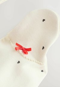 Knæhøje sokker i creme, med små sorte hjerte mønstre, en rød sløjfe accent ved kanten og en blød strikket tekstur.