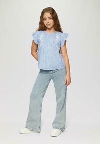 Hellblauses, gestreiftes Kurzarmoberteil mit floraler Stickerei, kombiniert mit hellen, weit geschnittenen Jeans und weißen Sneakers. Einfaches Design und Textur.