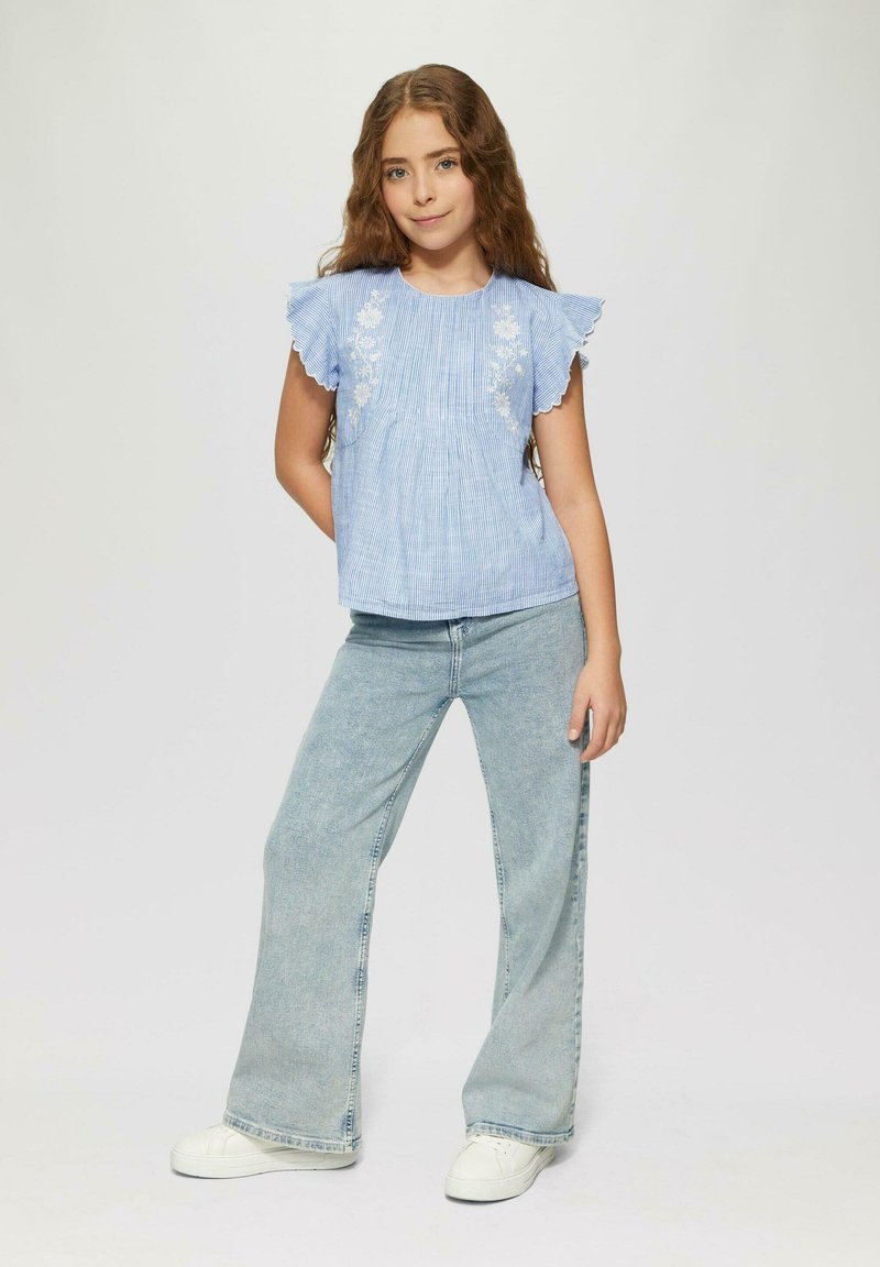 Hellblauses, gestreiftes Kurzarmoberteil mit floraler Stickerei, kombiniert mit hellen, weit geschnittenen Jeans und weißen Sneakers. Einfaches Design und Textur.