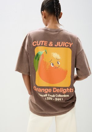 Bruine oversized t-shirt met een kleurrijke cartoonachtige oranje graphic. De tekst luidt "CUTE & JUICY" en "Orange Delights" in vette letters.