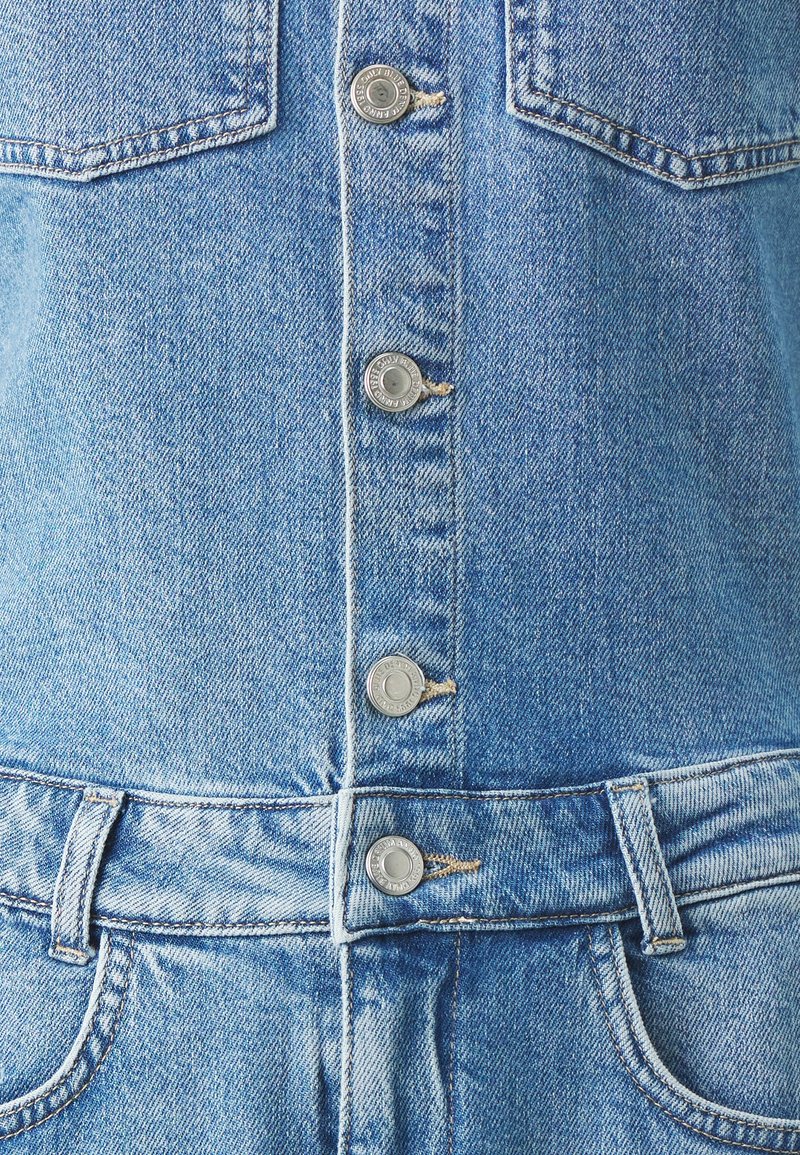 Light blue denim jumpsuit with five front buttons, two pockets, and a fitted waist. Distressed fabric texture, classic design with a casual appearance.