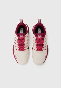 Beige sneakers med burgunder aksenter, mesh-overdel, snøring, og stripet pull-tabu. Har en teksturert gummisåle og logo.