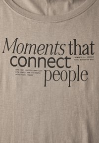 Camiseta de algodón gris con un texto negro destacado que dice "Momentos que conectan a las personas". El texto varía en tamaño y estilo de fuente.