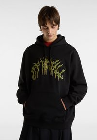 Černá mikina s kapucí vyrobená z měkké tkaniny, která má na přední straně velký, jasně zelený grafický design. Má přední kapsu a volnější střih.