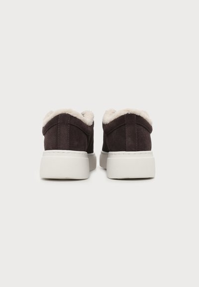 Chaussures en daim marron foncé à enfiler avec semelles épaisses blanches et doublure duveteuse couleur crème, vues de dos sur un fond uni.