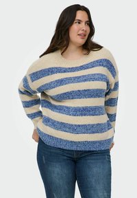 Gestreepte trui met brede blauwe en crèmekleurige strepen, gebreide textuur, ronde halslijn, verlaagde schouders en een relaxte pasvorm. Gecombineerd met blauwe jeans.