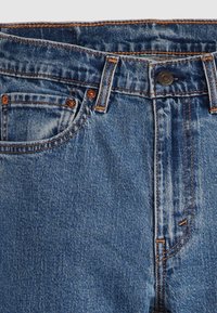 Blå denimjeans med en klassisk design, orange sömmar, knappstängning och detaljerade framfickor. Tyget har en lätt struktur.