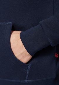 Granatowy hoodie z kieszenią z przodu, ściągaczami przy mankietach i gładką fakturą; posiada małe czerwone logo po prawej stronie.
