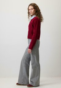 Czerwony sweter z splotem warkoczowym z dekoltem w serek i guzikami, w połączeniu z szarymi dżinsami o szerokich nogawkach. Strój uzupełniają bordowe zamszowe buty.