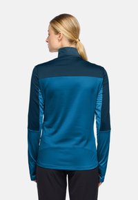 Maglia sportiva a maniche lunghe in due tonalità di blu, con colletto alto e texture liscia. Il design include un pannello posteriore a contrasto e una forma aderente.