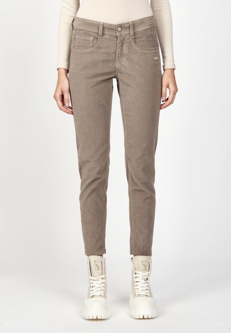 Brown corduroy pants with a slim fit, featuring front pockets and a button closure. Paired with white high-top sneakers. Plain background.