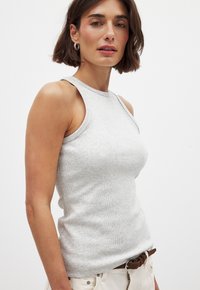Débardeur gris à côtes avec une coupe ajustée, sans manches, encolure ronde et texture subtile. Associé à une ceinture marron et un pantalon de couleur claire.