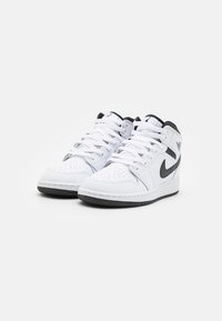 Fehér magas szárú sportcipők perforált lábujjjal, fekete részletekkel a swooshnál és texturált gumitalppal, fehér fűzőkkel és logó díszítésekkel.