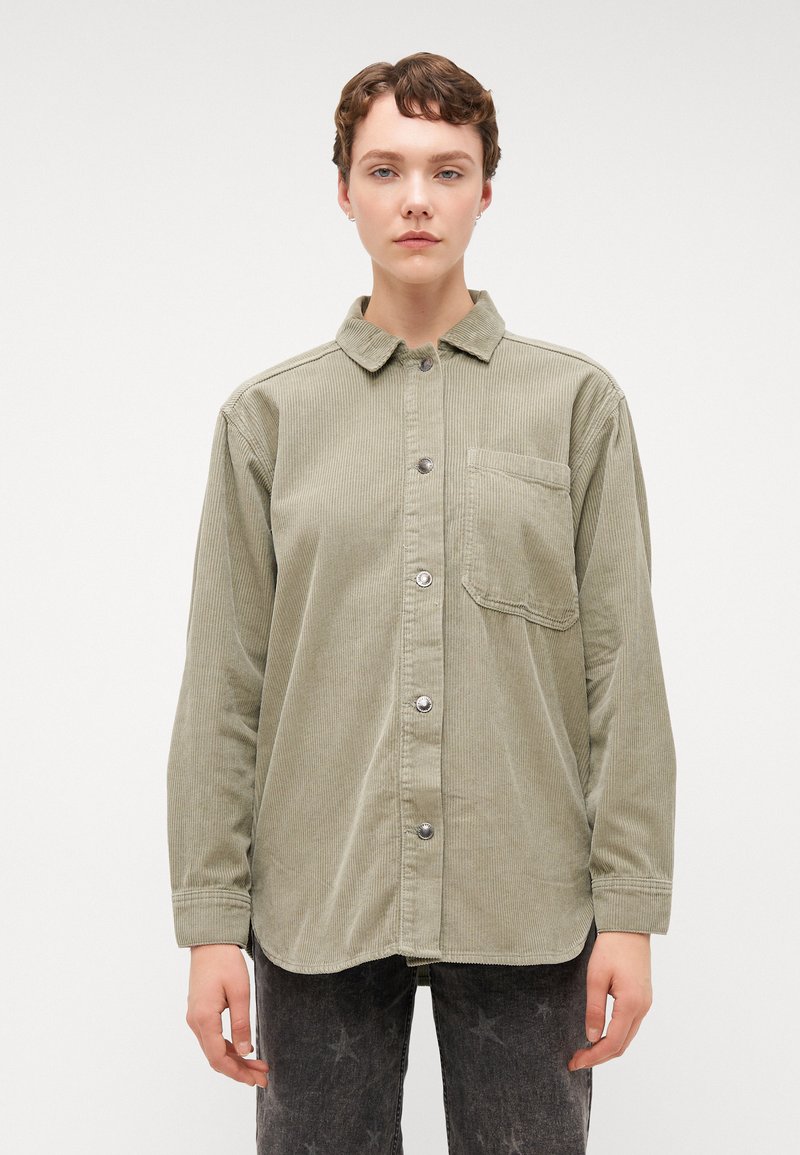 Chemise en velours côtelé vert avec col, manches longues et poche avant. Caractéristiques : boutons en métal argenté et tissu texturé.