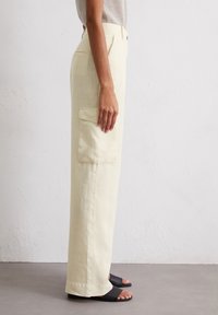 Helle gelbe Leinen-Cargohosen mit einer Seitentasche, gerader Schnitt und entspannter Passform. Tragen Sie dazu schwarze Sandalen mit offenem Zeh.