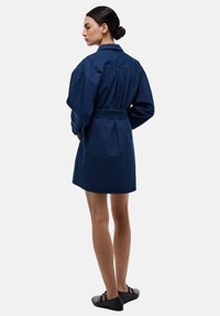 Robe en denim foncé avec ceinture, dotée de manches longues, d'un col et d'une coupe décontractée, avec une taille cintrée et un ourlet droit.