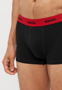 Schwarze Baumwollboxershorts mit einem roten elastischen Bund und "DIESEL"-Logo. Enganliegendes Design mit genähten Details.