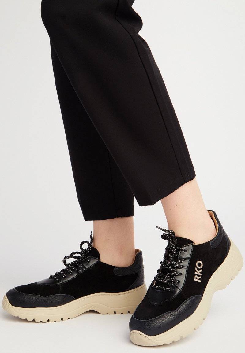 Czarne sneakersy wykonane z gładkiej skóry i zamszu, z grubą beżową podeszwą i czarnymi sznurówkami. Logo RKO z boku.