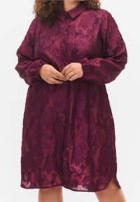 Punarumpu paita, joka on valmistettu läpikuultavasta kankaasta, jossa on kukkakuosi. Napitus edessä, kaulus ja pitkät puffihihat. Sivuslitit ja rento malli.