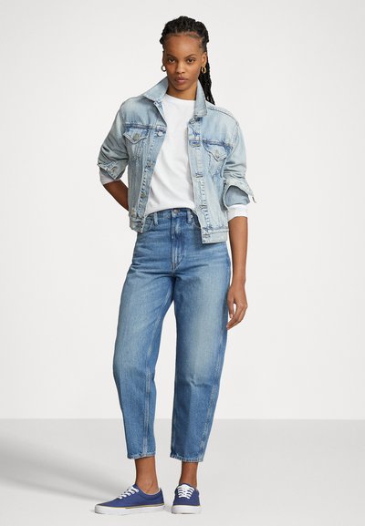 Helles Jeansjackett mit klassischem Design, getragen über einem weißen T-Shirt; kombiniert mit hellblauen, hochgeschnittenen Jeans und navyblauen Sneakers.