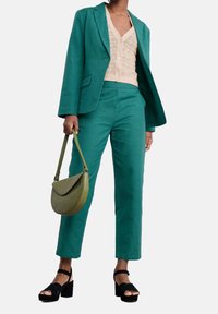 Zestaw marynarki i spodni w kolorze zielono-niebieskim, wykonany z teksturowanej tkaniny, połączony z kremowym sweterkiem. Dodatki to zielona torebka i czarne sandały na platformach.
