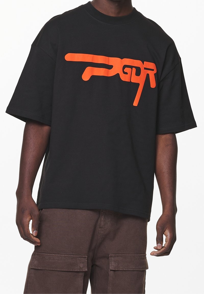 Black cotton T-shirt featuring a large orange graphic logo. Loose fit with short sleeves and a crew neckline. Simple, unembellished design.