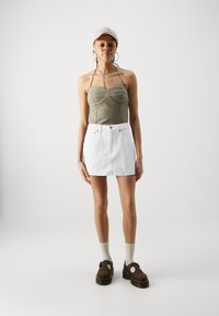 Haut bustier ajusté vert olive, mini jupe en denim blanche, chaussures à plateforme marron, casquette beige, boucles d'oreilles en argent, chaussettes en coton marron clair.