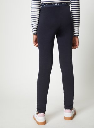 Leggings stretch bleu marine avec une texture lisse, dotés d'une taille de marque et d'une coupe ajustée, associés à des baskets blanches avec des accents roses.