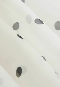 Tela blanca transparente con lunares negros de diferentes tamaños, textura suave, ligera, con pliegues delicados. Superficie lisa con un brillo sutil.