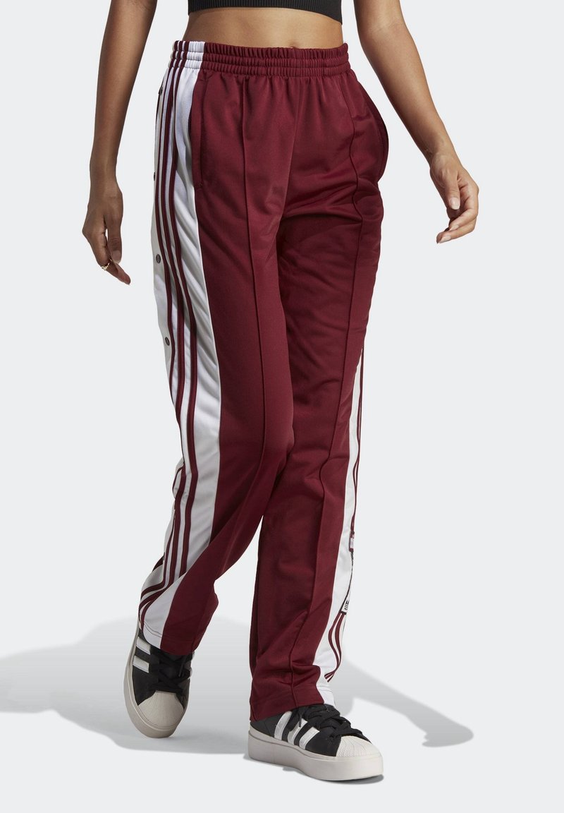 Maroon track pants with white side stripes, elastic waistband, and snap-button detail along the sides. Paired with black and white sneakers.