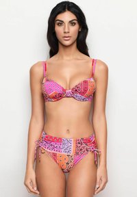 Bikini med rosa och orange bandana-mönster med justerbara remmar och sidoknytning. Toppen har en rosettdetalj i mitten.