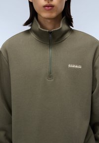 Oliven grøn, sweatshirt med kvart lynlås lavet af blødt stof, med høj krave og et logo mærke på venstre bryst. Glat tekstur, afslappet pasform.