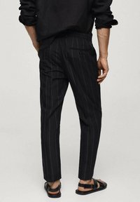 Pantaloni a strisce nere con vestibilità sartoriale, realizzati in tessuto leggero. Comprendono una tasca posteriore e gambe leggermente svasate.