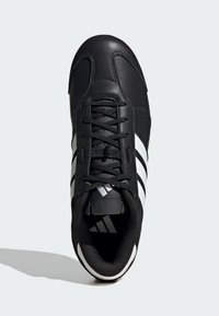 Svart sportskor med slät läderöverdel, kontrasterande vita, kantiga ränder, snörning och perforerade detaljer längs sidorna.