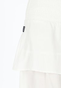 Weißes Top mit einem gerafften Design und einem unteren Rüschensaum. Enthält ein kleines Label "SEASIDE" an der Seite. Weiche Textur und leichtes Material.